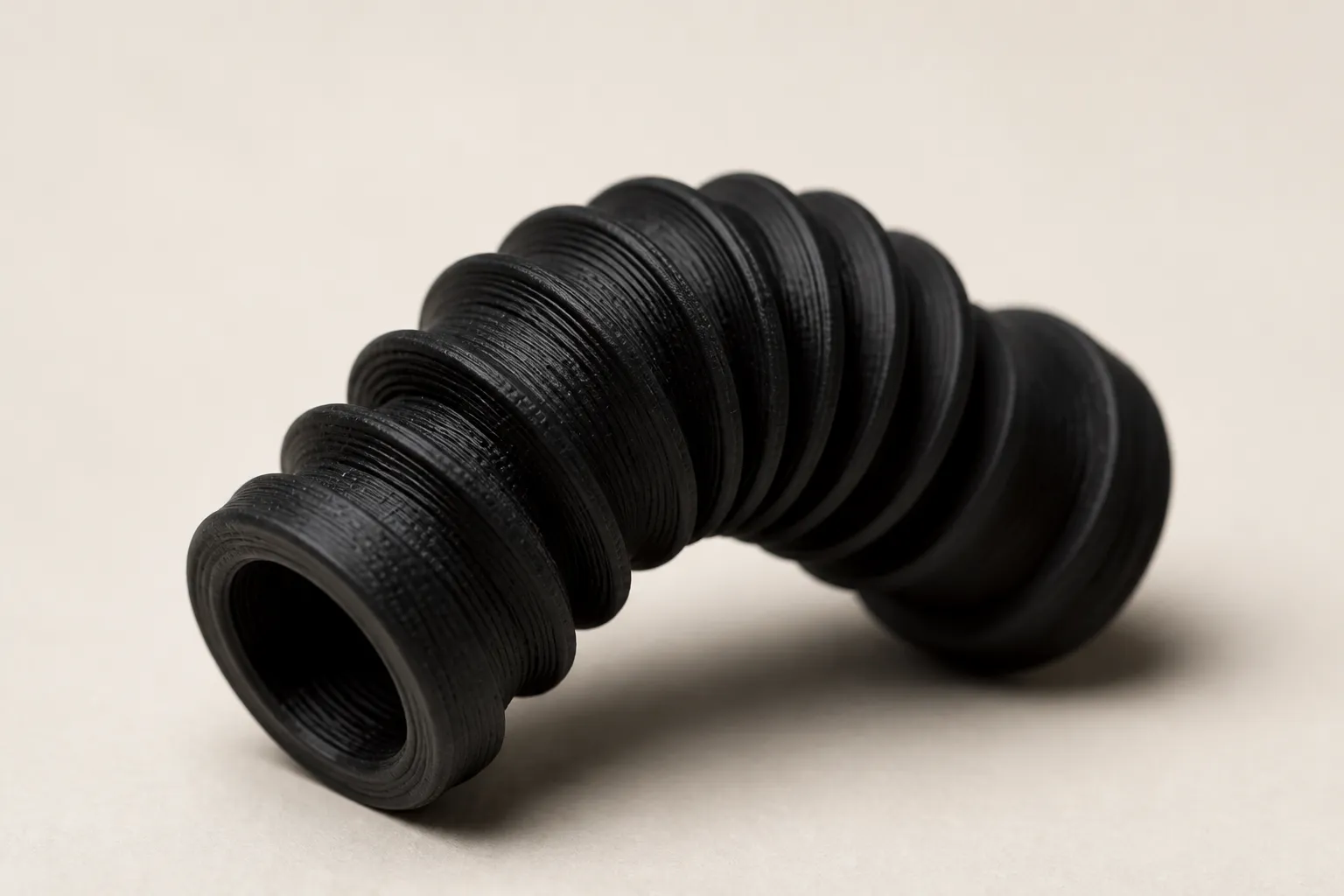 A matte black TPU bellows bent into a curve, with visible FDM layer lines.